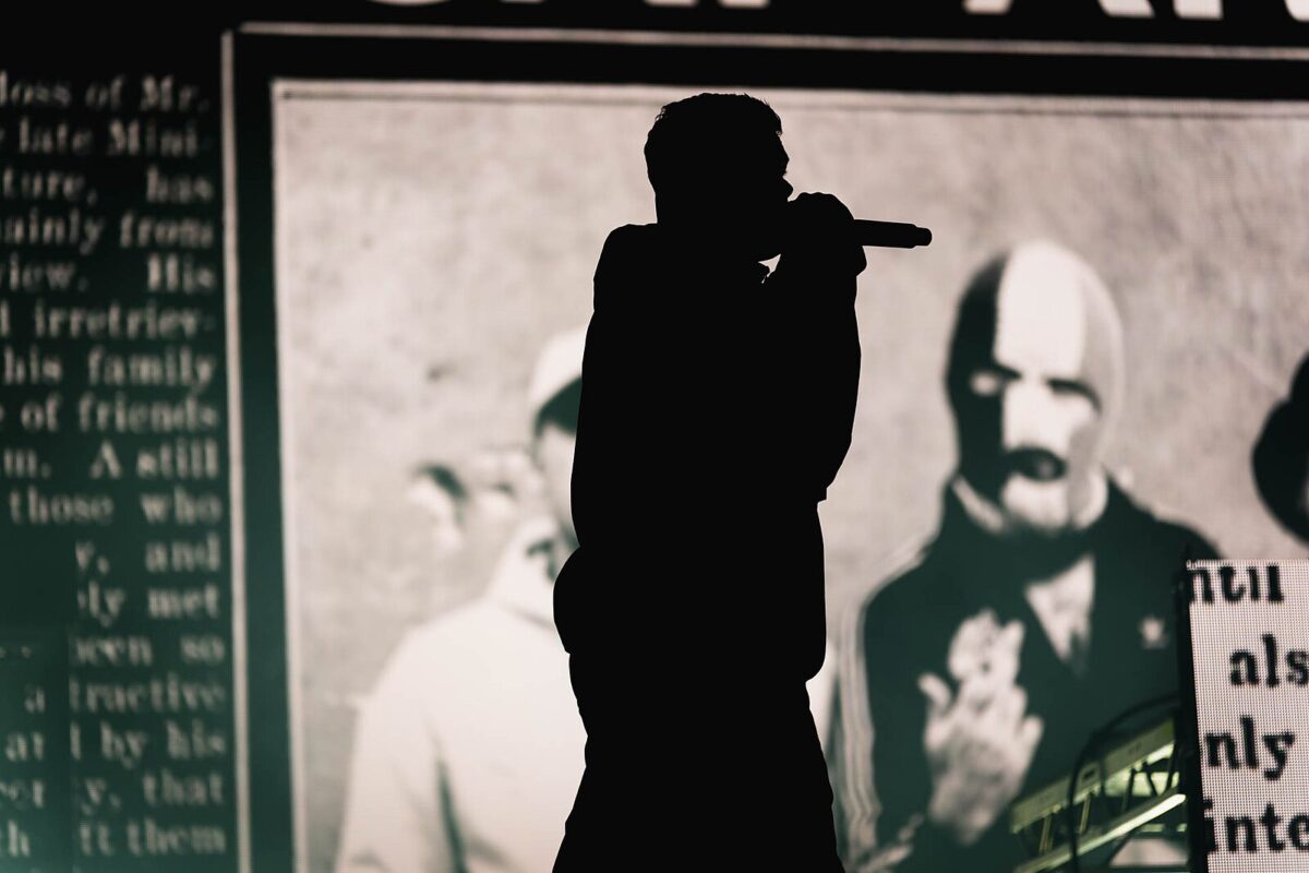 Silhouette of Kneecap singer Mo Chara against black and white image of the band in the background