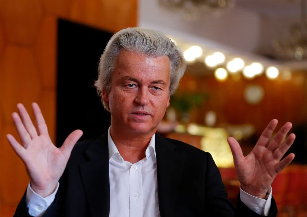 Geert Wilders with his hands spread wide as if he is describing something to the camera. He looks like a magician or scam artist.