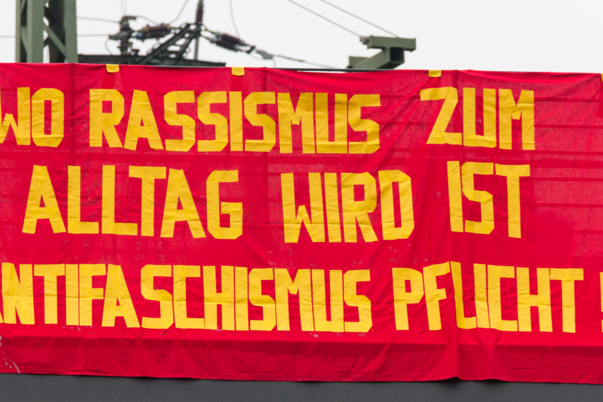 Large red and yellow banner which reads "Wo Rassismus zum Alltag wird ist Antifaschismus pflicht!" (Where racism becomes commonplace, antifascism is a duty!)